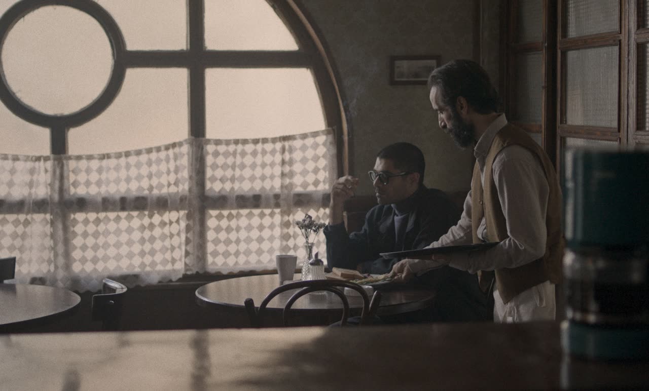 A man sits at a table by an arched café window