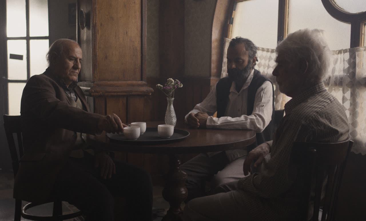 Three men talk around a café table