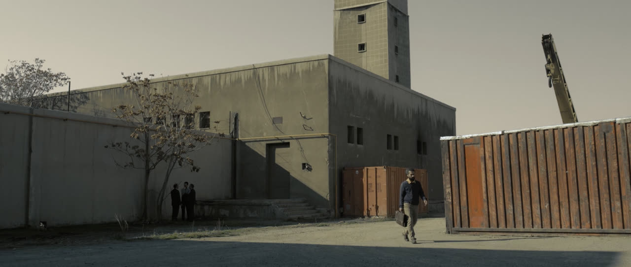 A man walks past an old factory building and rusted containers