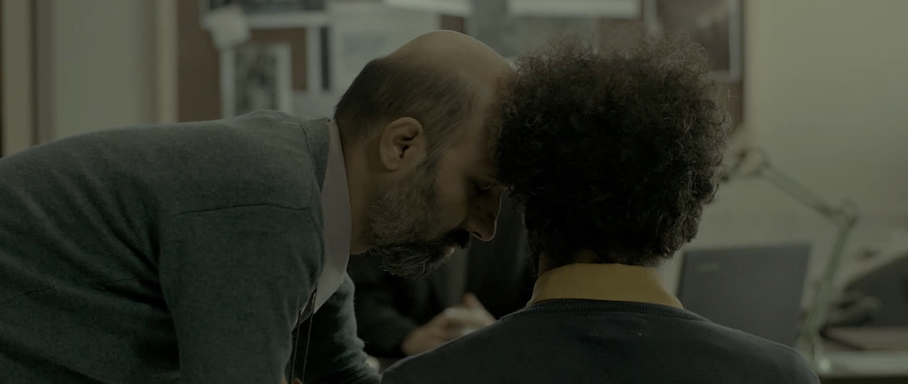 Two men lean close together in an office
