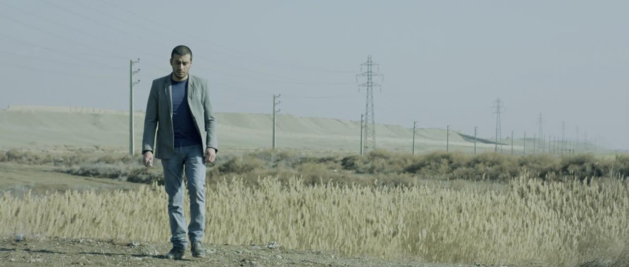A man in a jacket stands in a dry field