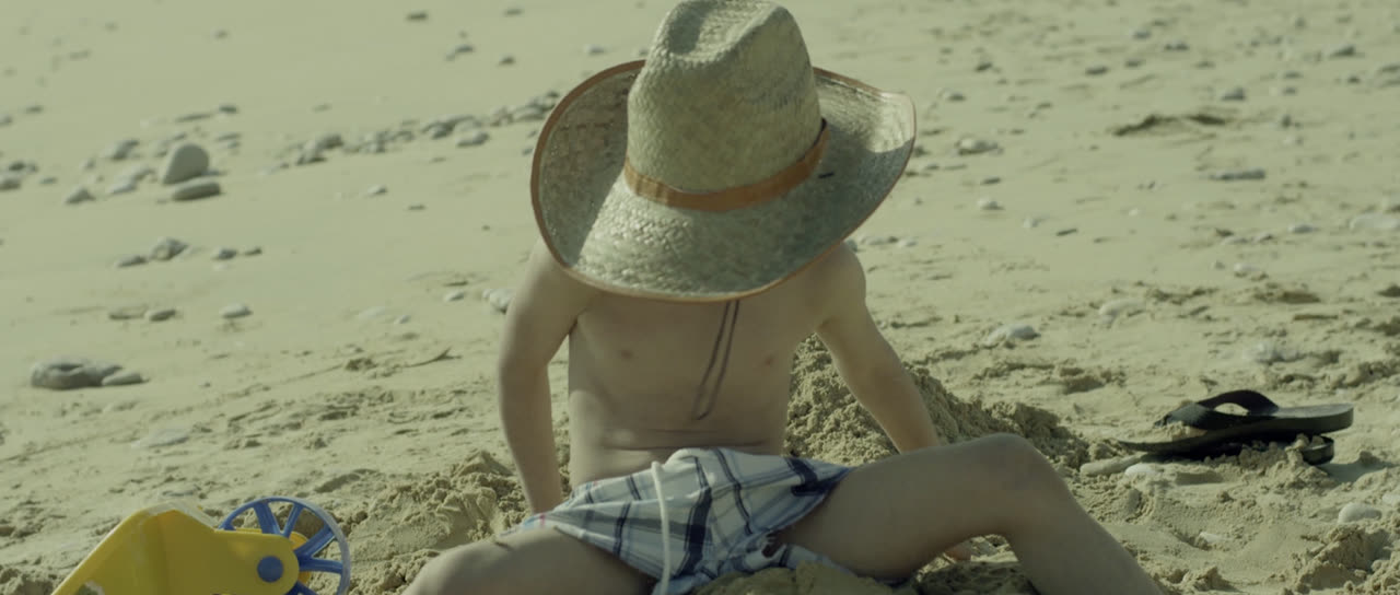 A child in a straw hat plays in the sand