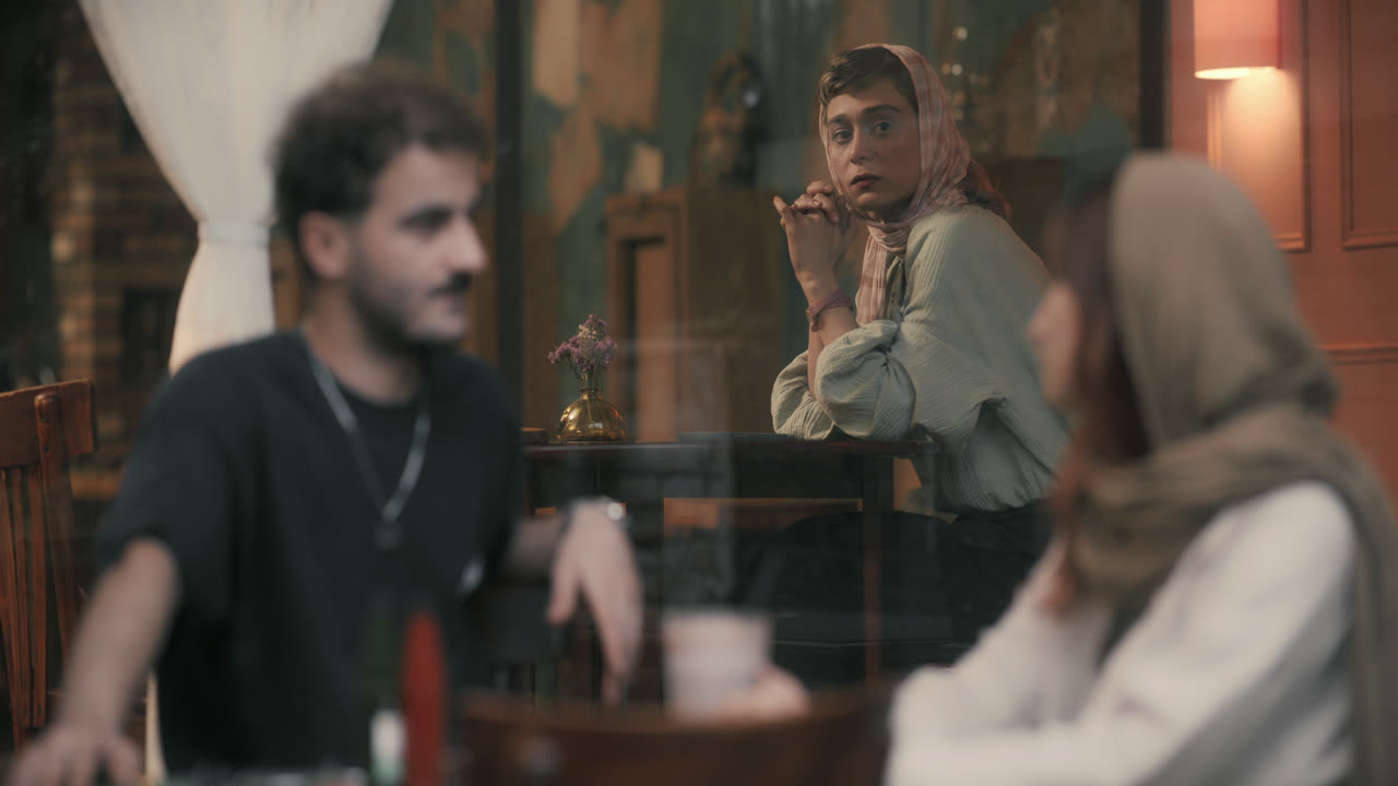 A man and a woman talk at a café table while another woman watches