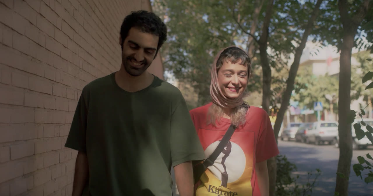 A young man and woman laugh as they walk down a tree-lined street
