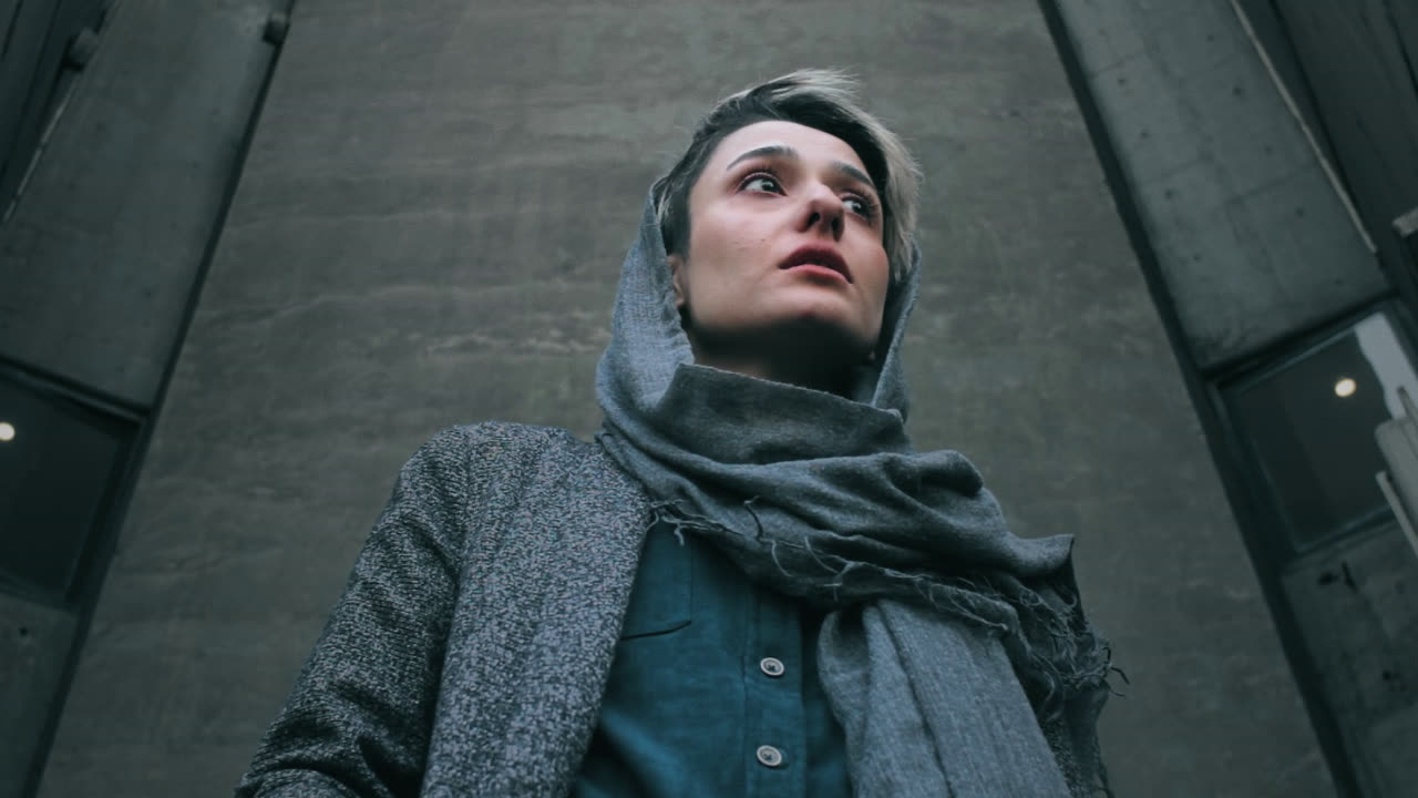 A woman in a headscarf looks up from a concrete passage